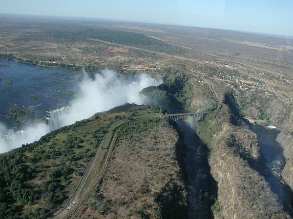 "Here's a view of Victoria Falls from the helicopter. (You'll probably want to click the image to see a larger picture, where you'll find this caption waiting for you at the bottom.) At the left the broad Zambezi plunges 100 metres into the first gorge, raising the eternal cloud of mist and forming a rainbow visible in front of the bridge across the gorge. We're overflying Zimbabwe at the moment; the "Knife Edge" from which the first photo of the falls above was taken protrudes from the Zambia side above and to the left of the bridge. The bungee jumping platform is visible at the centre of the bridge, near the top of the rainbow. Electricity generation in Zambia is in excess of 99% hydroelectric; a power station is visible at the right of the image, along with outflow from the turbines into the gorge. After the falls, the Zambezi traverses a series of zigzag gorges, the first two of which are visible here." Photo and words by John Walker (2001)